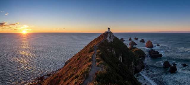 Nugget Point Ein Leuchtturm auf einer Klippe über dem Ozean bei Sonnenuntergang