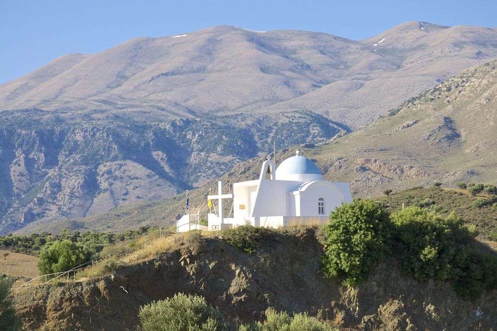 Eine weiße Kirche mit einer blauen Kuppel sitzt auf einem Hügel mit Bergen im Hintergrund