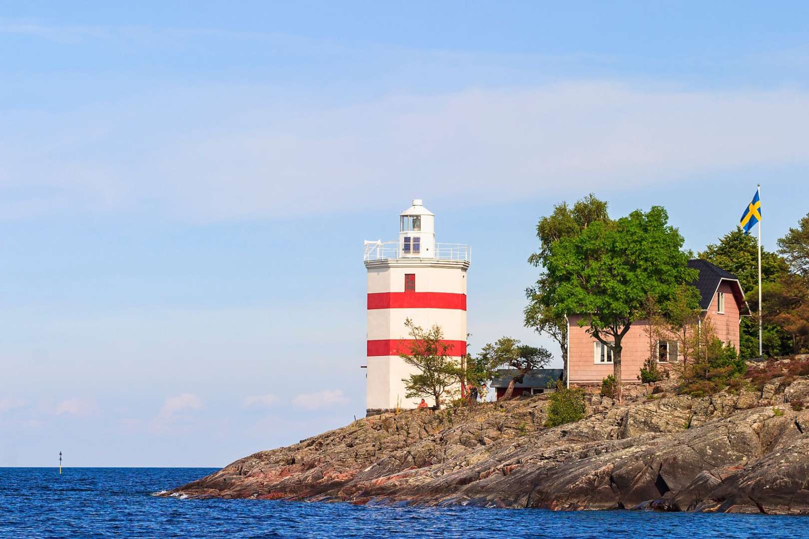 Ein rot-weißer Leuchtturm steht auf einem felsigen Ufer neben einem rosa Haus