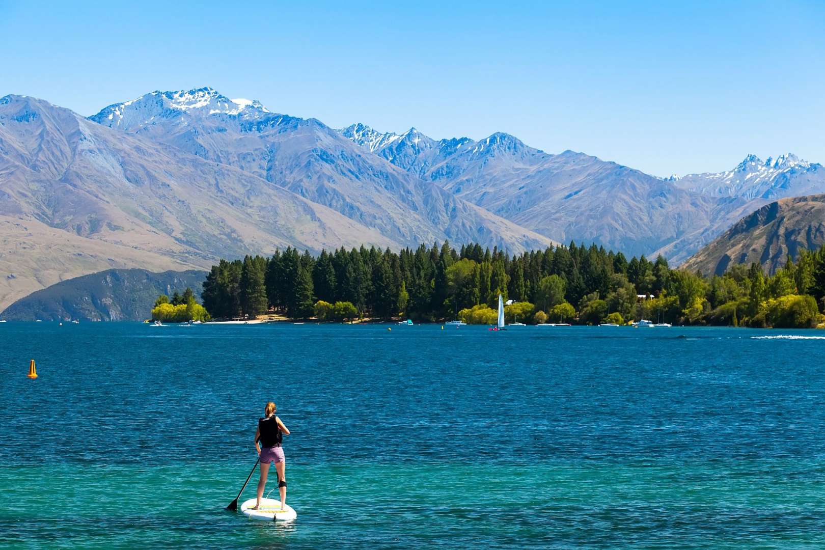 Ein Mann steht auf einem Paddleboard im Wasser mit Bergen im Hintergrund