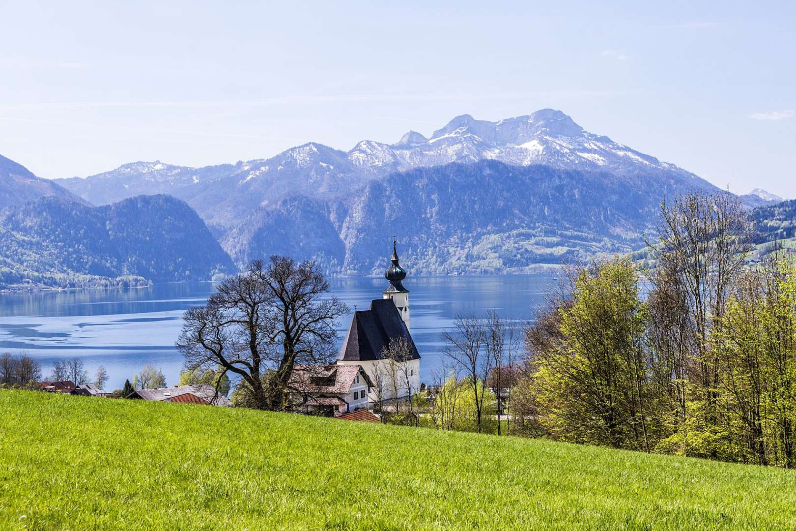 Eine Kirche steht auf einem Hügel mit Blick auf einen See mit Bergen im Hintergrund