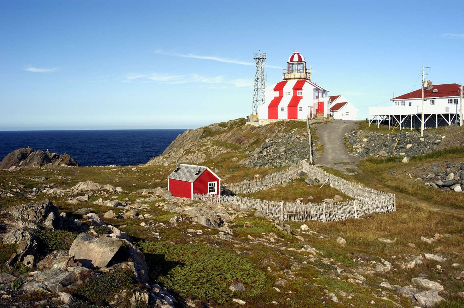 Ein rot-weiß gestreifter Leuchtturm steht auf einem felsigen Hügel in der Nähe des Ozeans