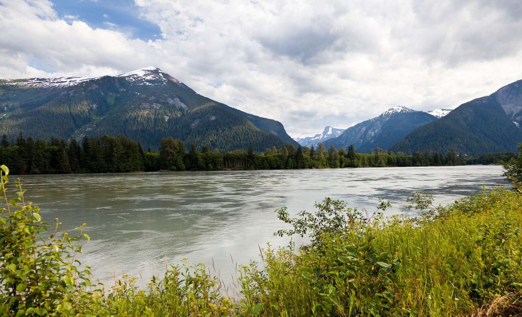 Ein Fluss mit Bergen im Hintergrund und Bäumen im Vordergrund