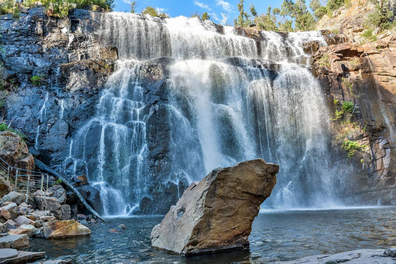Ein Wasserfall mit einem großen Felsen im Vordergrund