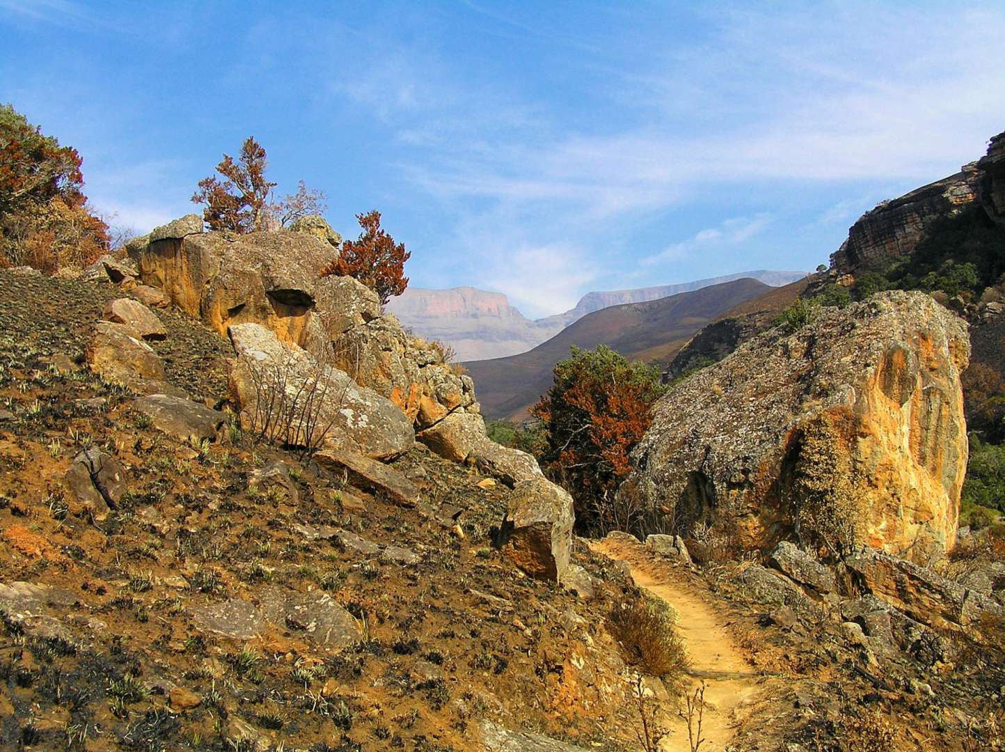 Ein Pfad führt durch eine felsige Landschaft mit einem Berg im Hintergrund