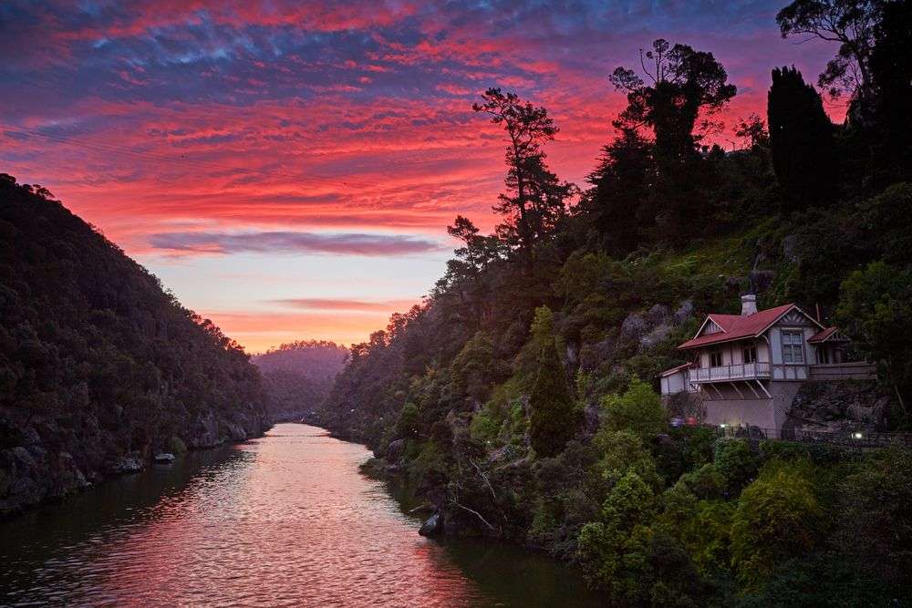 Ein Haus steht an einem Fluss mit einem Sonnenuntergang im Hintergrund