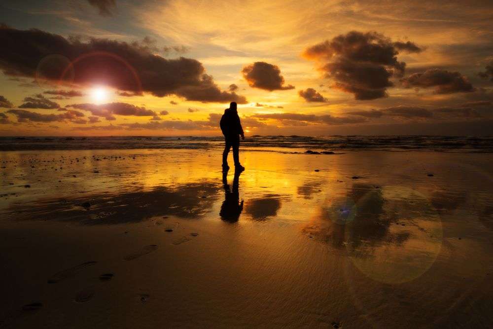 Eine Person steht am Strand und schaut auf den Sonnenuntergang