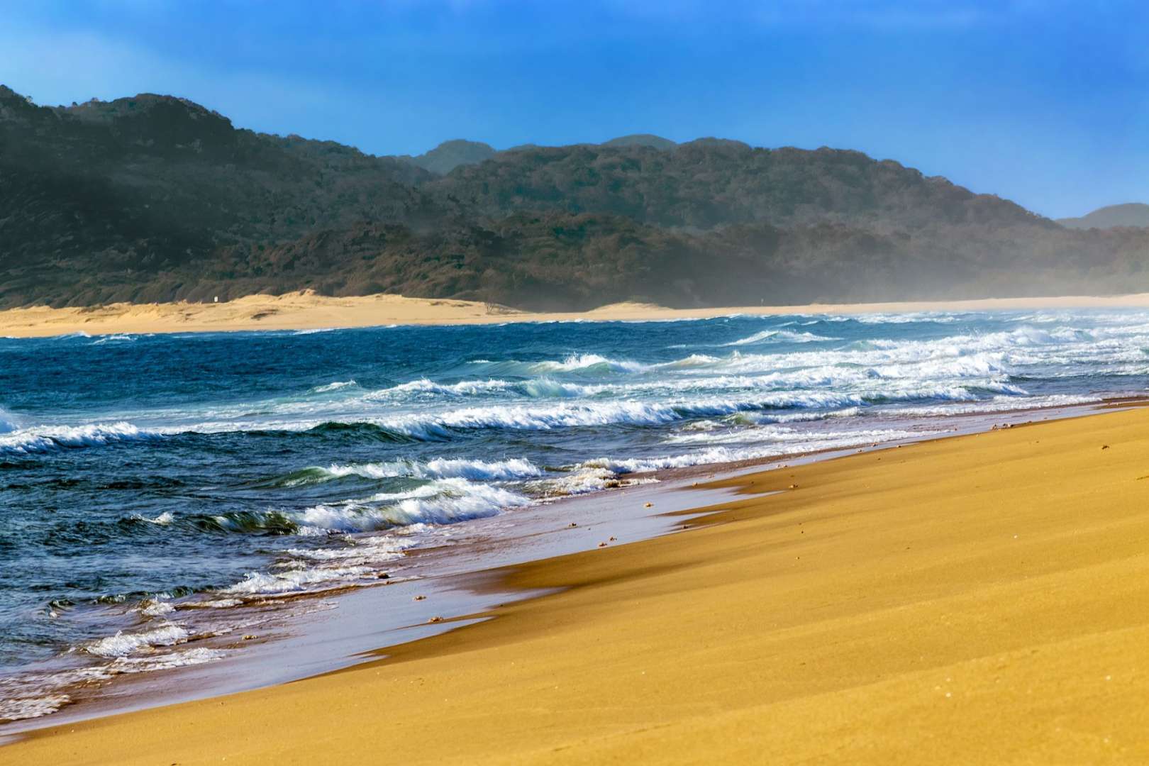 Wellen brechen an einem Strand mit Bergen im Hintergrund