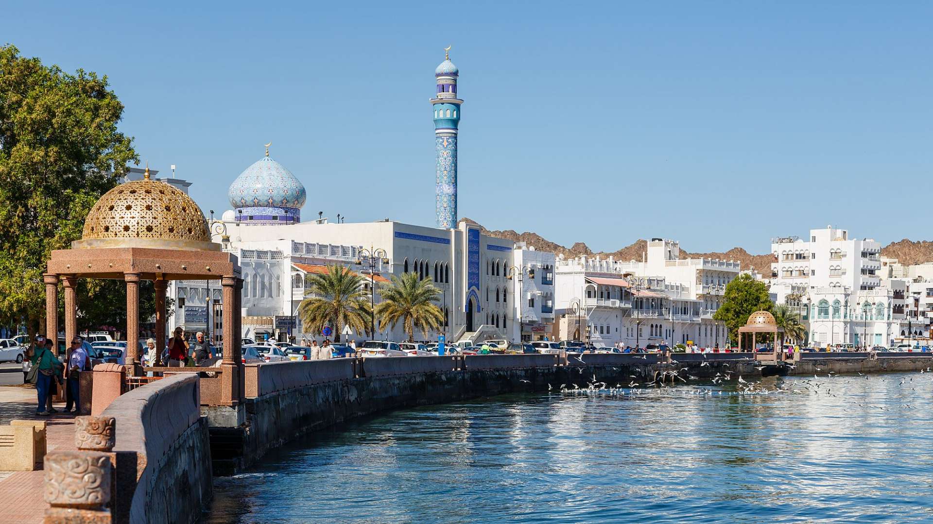 Eine Moschee mit einem blauen Minarett steht neben einem Fluss