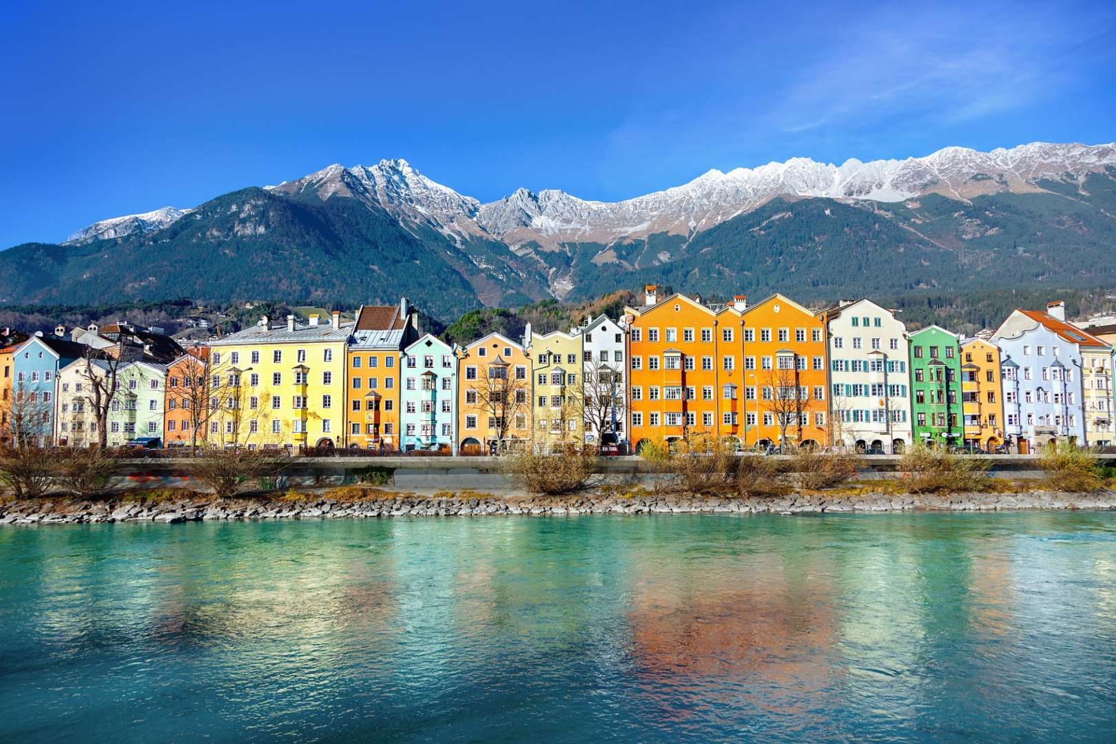 Eine Reihe von bunten Gebäuden neben einem Fluss mit Bergen im Hintergrund