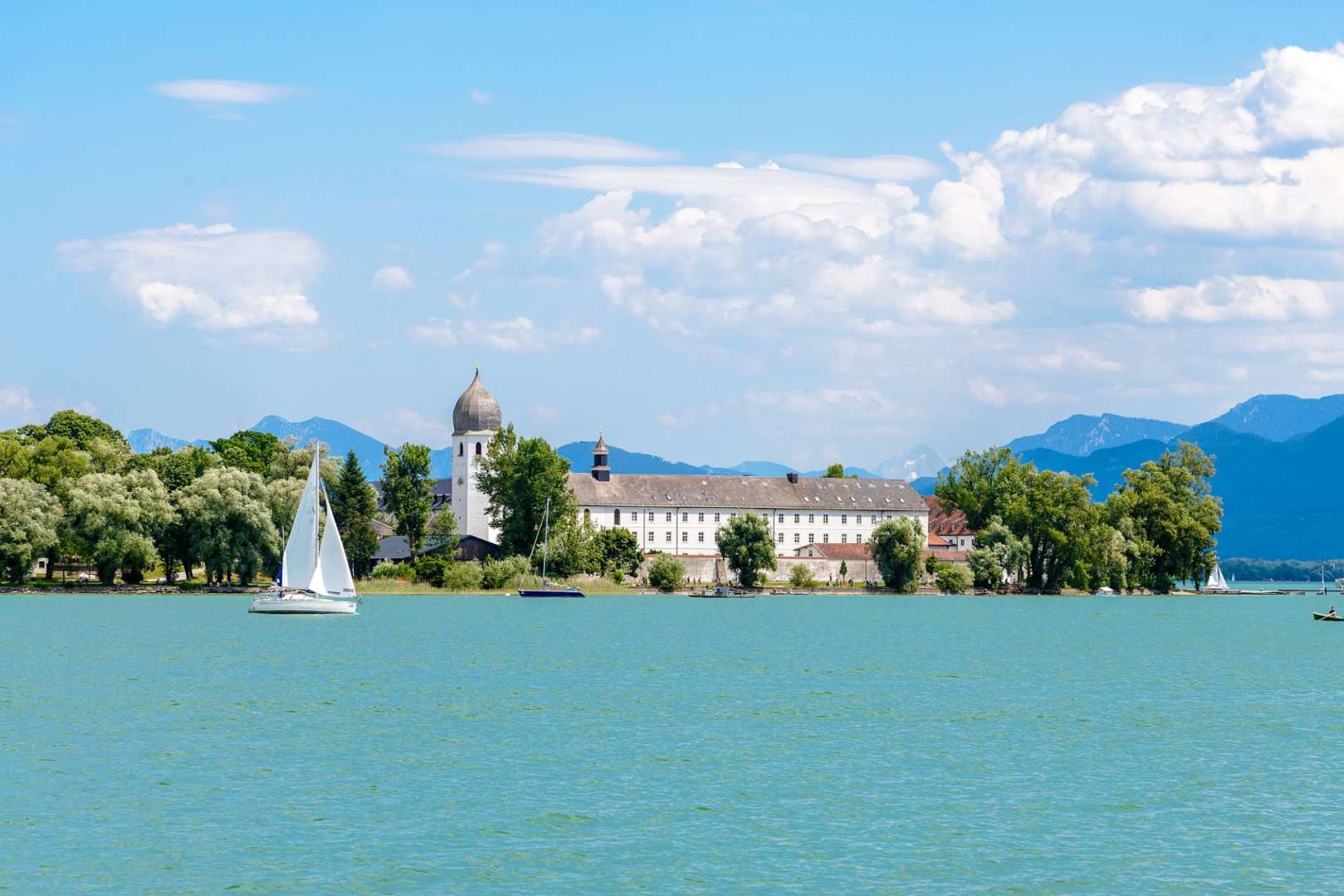 Ein weißes Segelboot schwimmt auf einem See mit einem großen Gebäude im Hintergrund