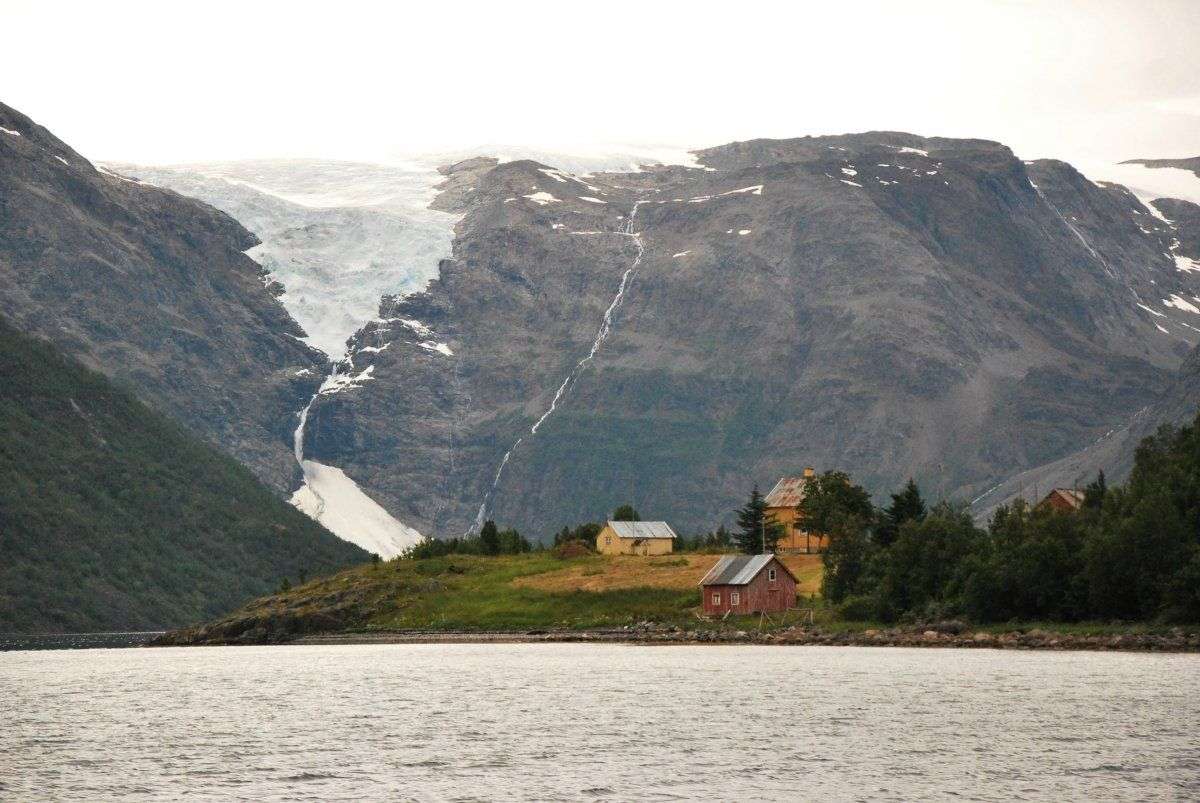 Ein kleines rotes Haus steht am Ufer eines Sees vor einem schneebedeckten Berg