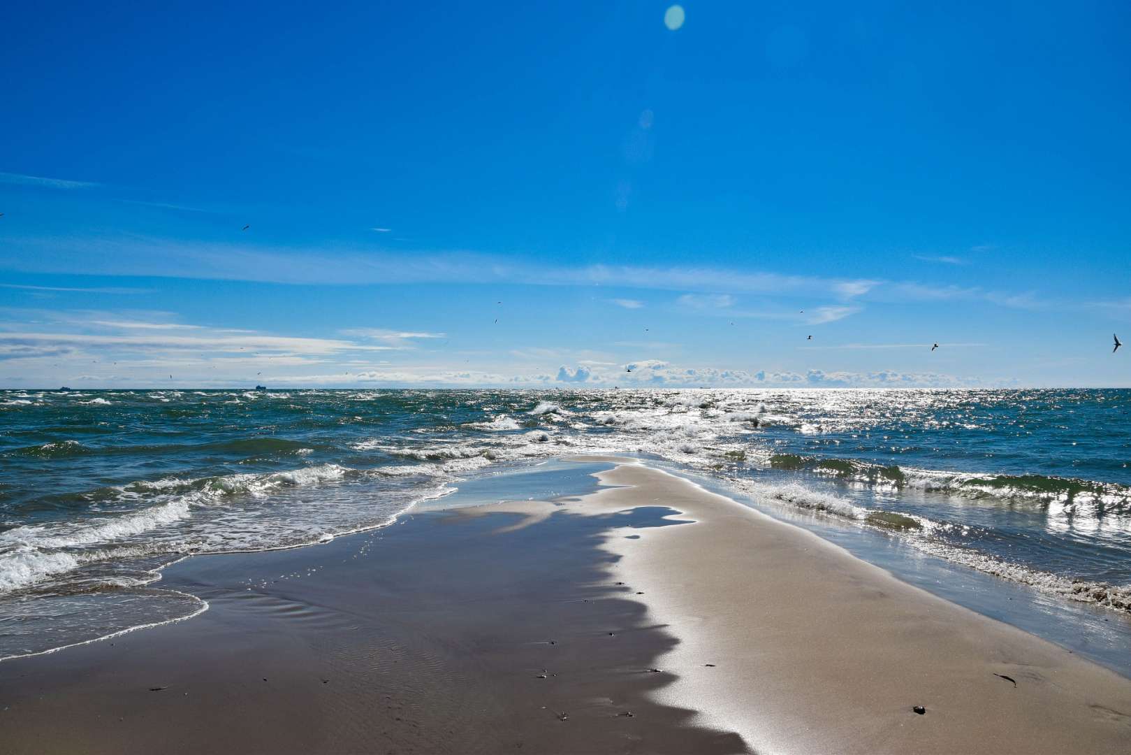Wellen brechen an einem sandigen Strand an einem sonnigen Tag