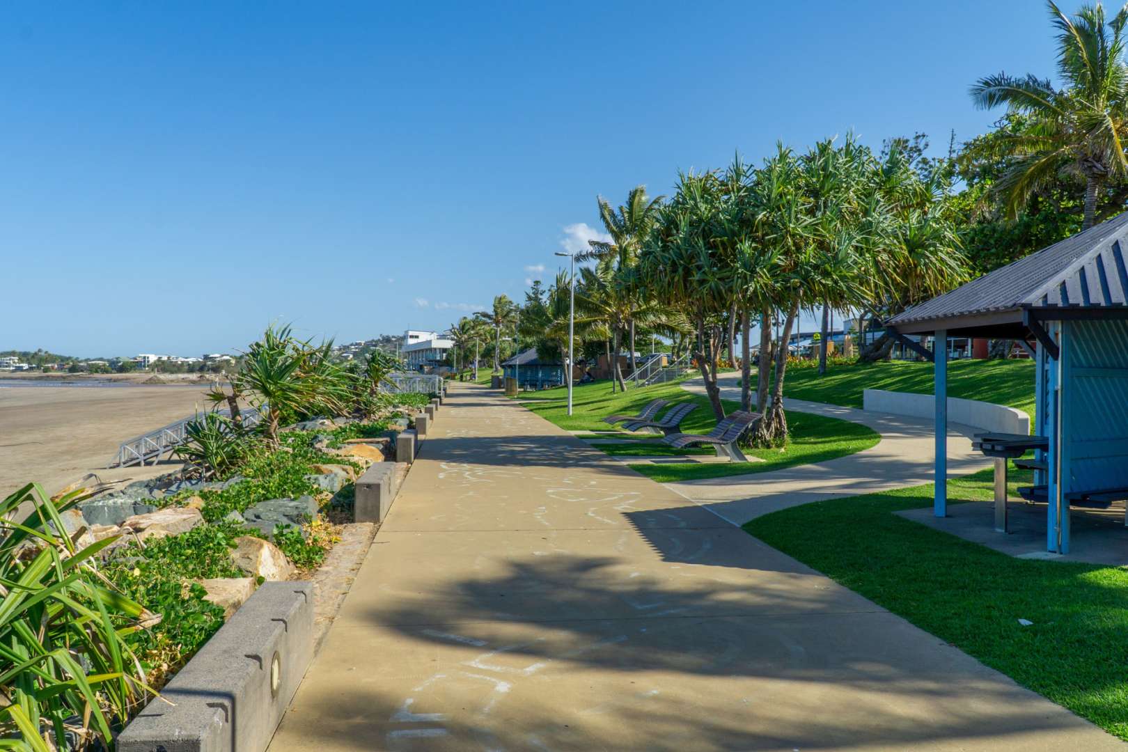 Ein Gehweg an einem Strand mit Bänken und Palmen
