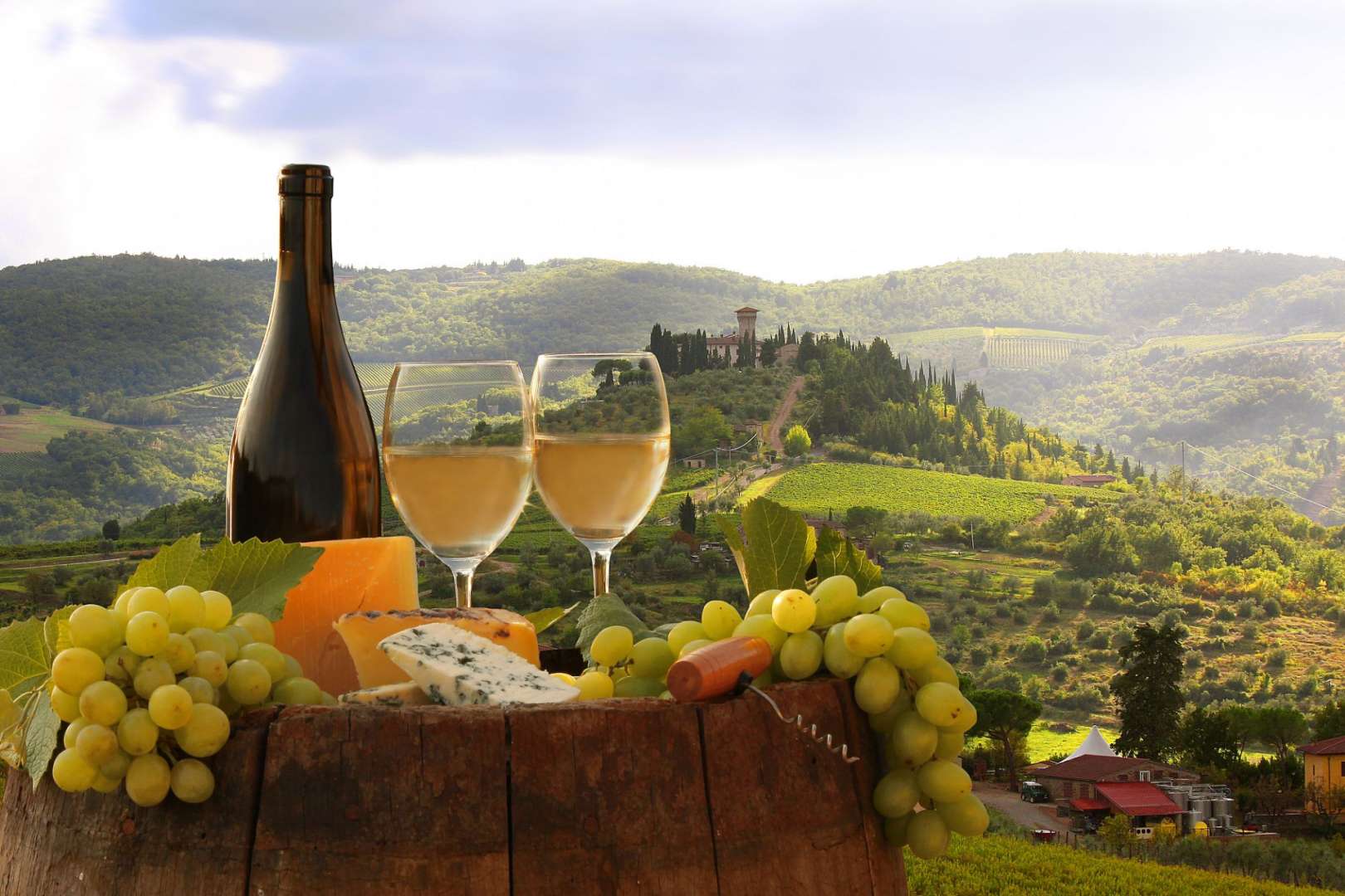 Zwei Gläser Wein stehen auf einem Holzfass mit Trauben und Käse