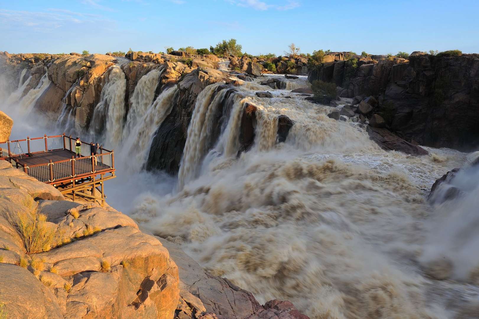 Ein Mann steht auf einem Holzsteg in der Nähe eines Wasserfalls