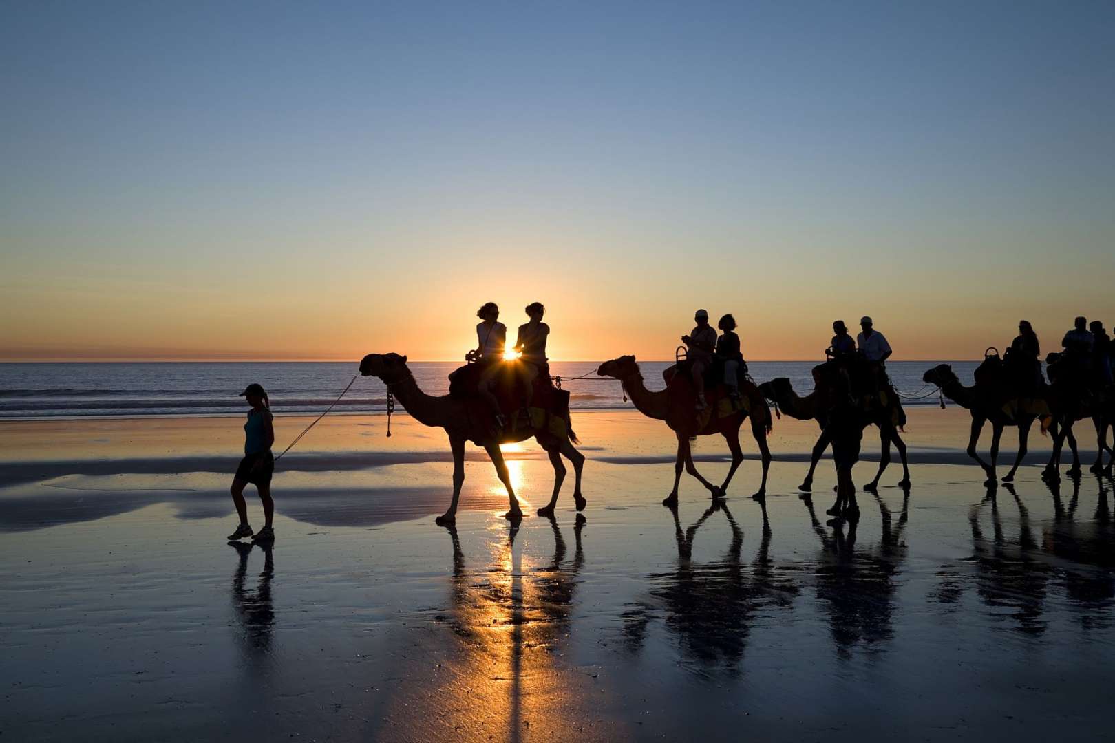 Eine Gruppe von Menschen, die auf Kamelen am Strand reiten