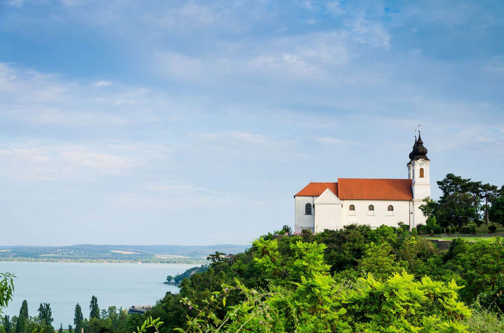 Eine kleine weiße Kirche auf einem Hügel mit Blick auf einen See