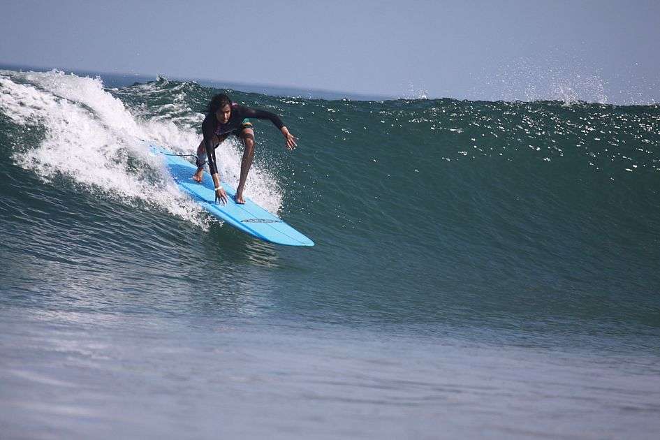 Ein Surfer fährt auf einem blauen Surfbrett eine Welle hinunter