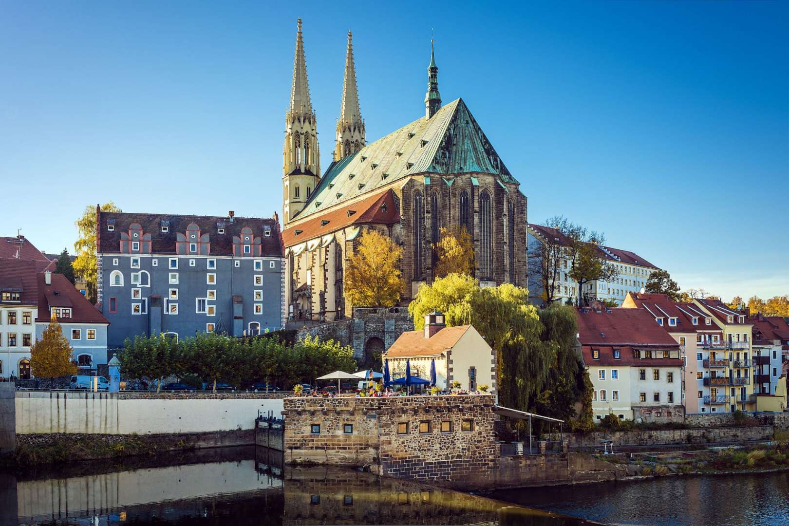 Eine große Kirche mit zwei Türmen steht in einer kleinen Stadt neben einem Fluss