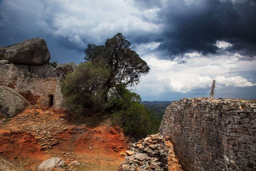 Eine steinmauer mit einem baum und einem großen felsen im hintergrund