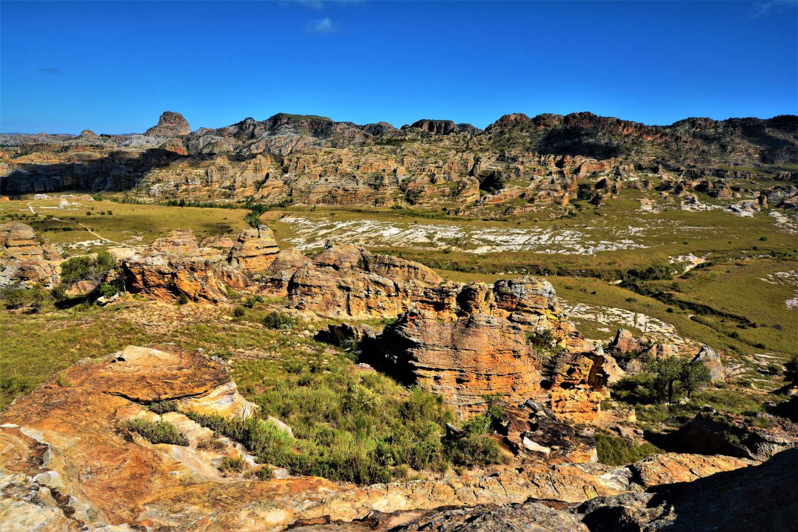 Ein weites Landschaftspanorama in Madagascar mit zerklüfteten Felsformationen und grünen Tälern unter einem strahlend blauen Himmel.
