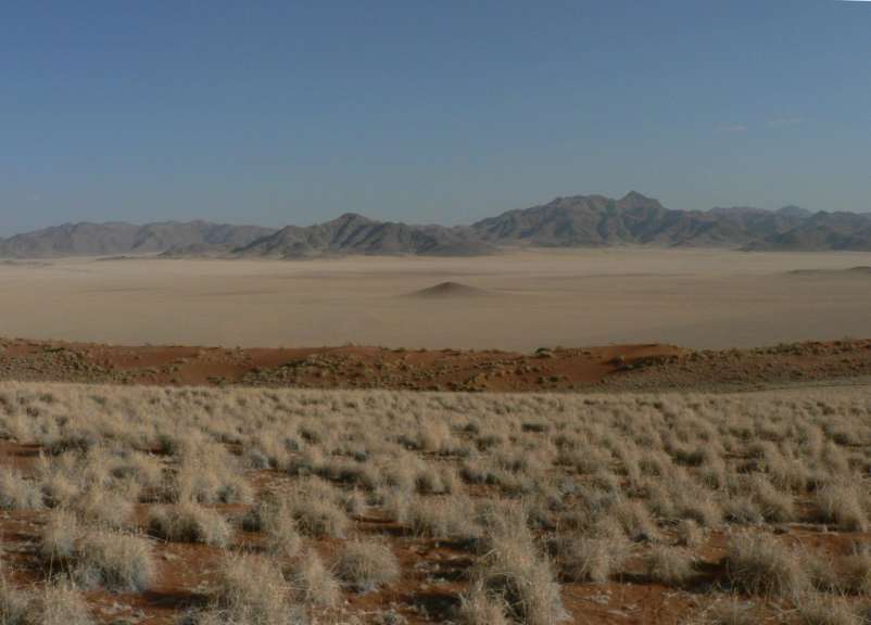 Eine Wüste mit Bergen im Hintergrund und Staub im Vordergrund