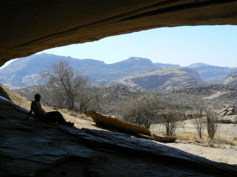 Ein Mann sitzt in einer Höhle mit Blick auf die Berge