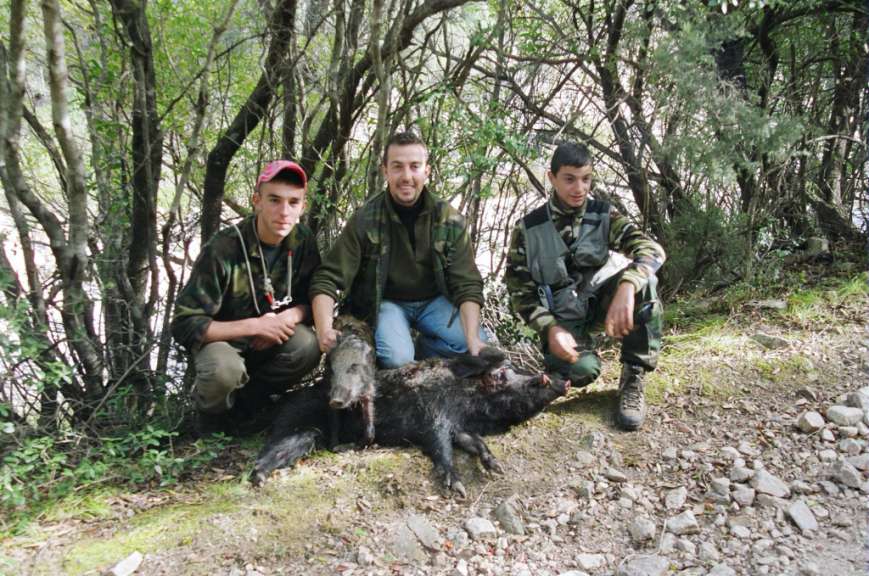 Drei Männer sitzen neben einem toten Schwein in einem Wald