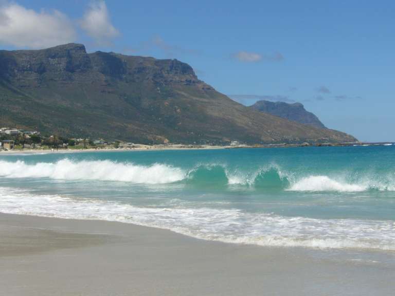 Wellen brechen an einem Strand mit Bergen im Hintergrund