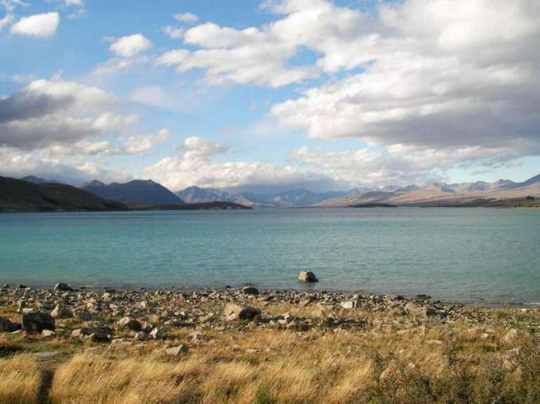 Ein See mit Bergen im Hintergrund und einem felsigen Ufer