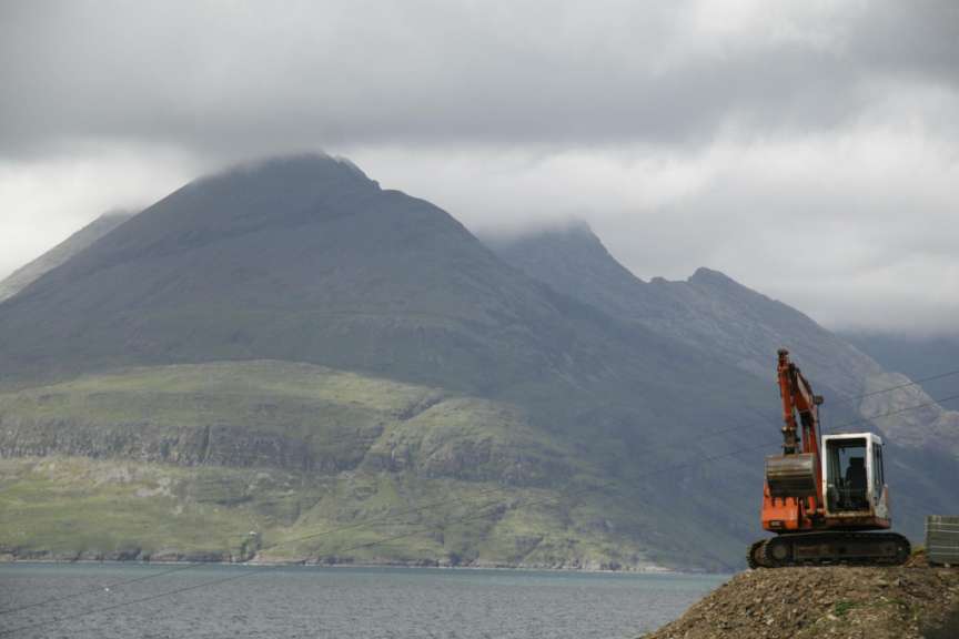 Ein orangefarbener Traktor sitzt auf einem Hügel mit einem Berg im Hintergrund