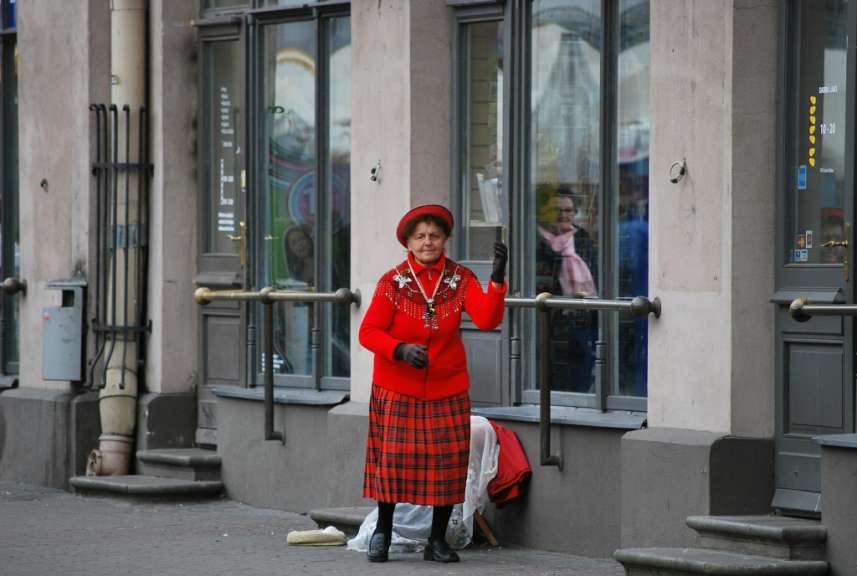 Eine Frau in einem karierten Rock und einer roten Jacke steht vor einem Gebäude