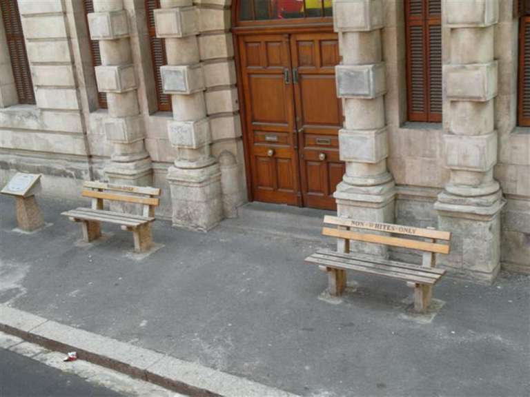 Zwei Bänke stehen vor einem Gebäude und weisen darauf hin, dass nur Stimmzettel verwendet werden dürfen