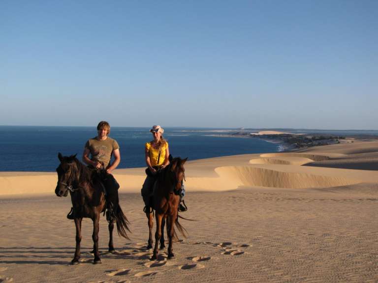 Ein Mann und eine Frau reiten auf Sanddünen in der Nähe des Ozeans