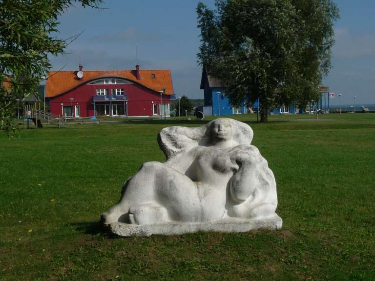 Eine Statue einer Frau liegt im Gras vor einem rosa Haus
