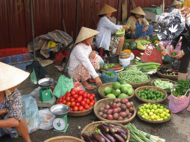 Eine Frau sitzt auf einem Markt und hält einen Korb mit Tomaten in der Hand