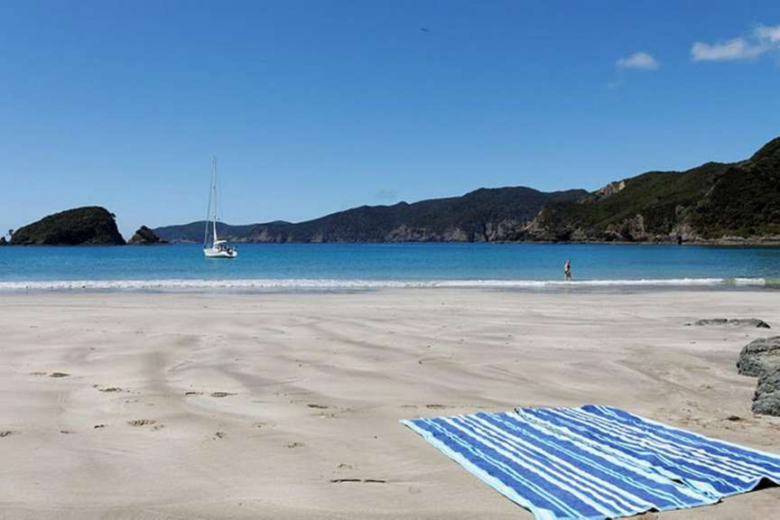Ein Strand mit einem blau-weiß gestreiften Handtuch und einem Boot im Hintergrund