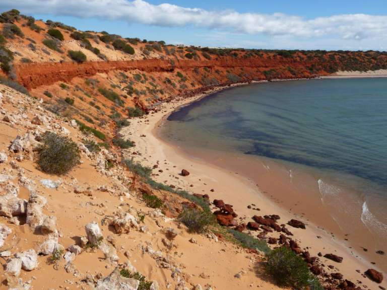 Ein Strand mit rotem Sand und blauem Wasser