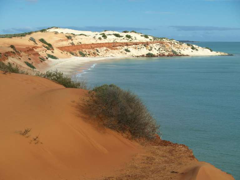 Ein Strand mit roten Sanddünen und einem blauen Ozean dahinter