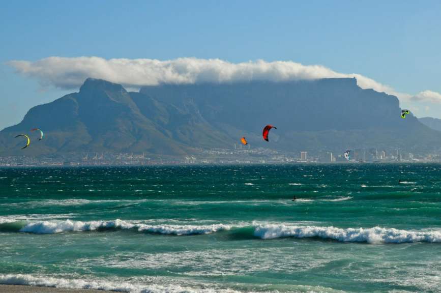 Eine Gruppe von Windsurfern fliegt über das Meer mit einem Berg im Hintergrund