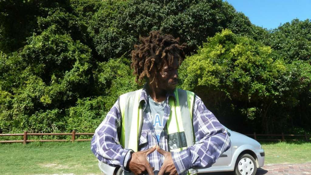 Ein Mann mit dreadlocks steht vor einem Auto