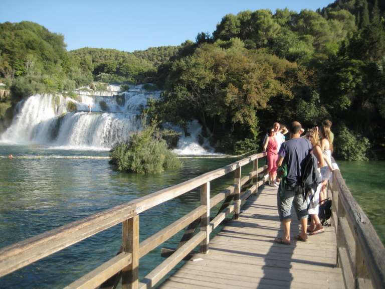 Eine Gruppe von Menschen steht auf einer Holzbrücke in der Nähe eines Wasserfalls