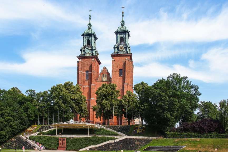 Auf diesem Bild ist die zweitürmige Backsteinkirche mit einer begrünten Anlage mit Blumenrabatten und Treppen im Vordergrund zu sehen.