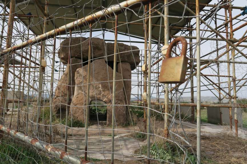 Ein versperrtes prähistorisches Steingebilde mit einem verrosteten Vorhängeschloss in der Vordergrund.