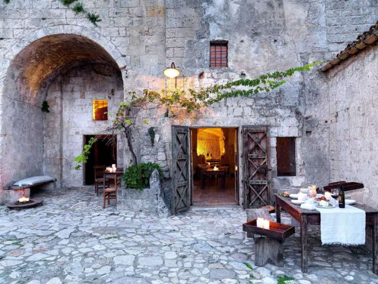 Ein Innenhof mit antiker Architektur und beleuchteten Tischen für ein Abendessen.