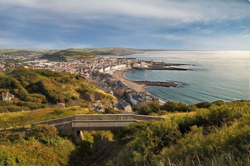 Ein Panoramablick von einem Hügel über eine Stadt am Meer mit einer Eisenbahnbrücke im Vordergrund.