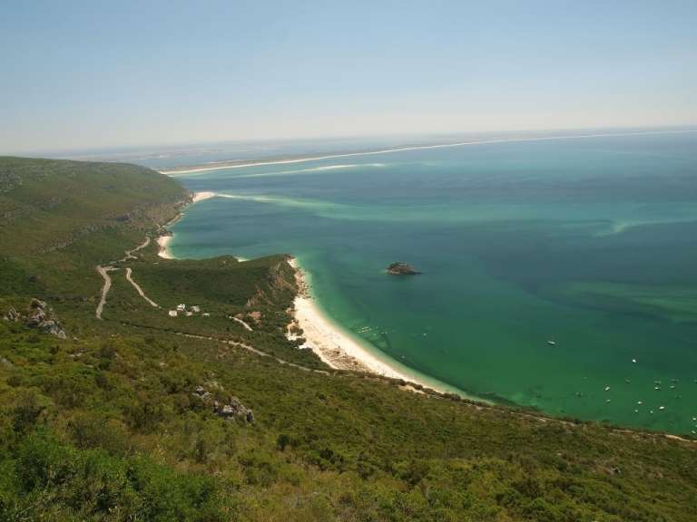 Ein Luftbild zeigt eine grüne Küste mit einem breiten Sandstrand und türkisfarbenem Wasser.