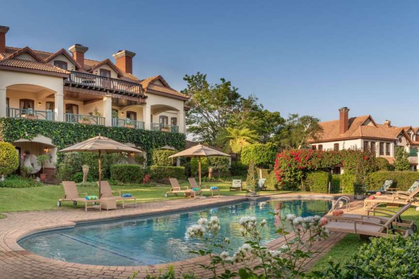 Ein luxuriöser Poolbereich mit Liegestühlen und Sonnenschirmen wird von einer großen Villa und üppiger Vegetation umgeben.