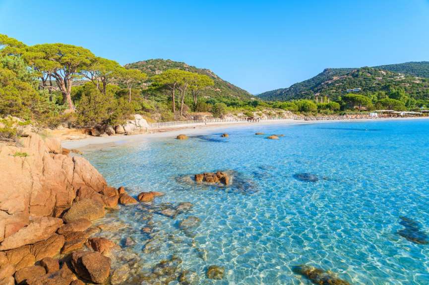 Ein ruhiger blauer Strand mit einer Reihe von Bäumen und Bergen im Hintergrund.